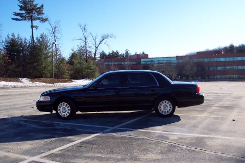 2001 Ford Crown Victoria - A black 2001 Ford Crown Victoria is parked in an empty lot on a sunny day.