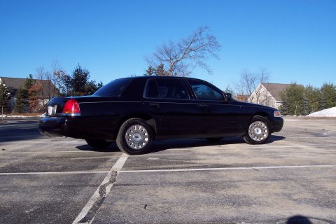 2001 Ford Crown Victoria - A black 2001 Ford Crown Victoria is parked in an empty lot under a clear blue sky.
