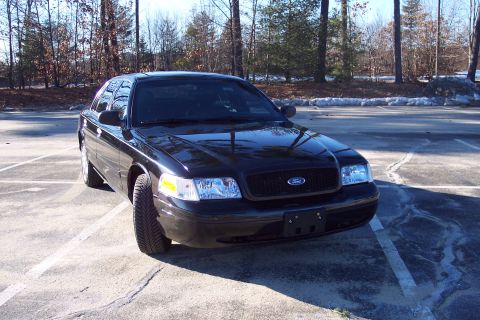 2001 Ford Crown Victoria - This black 2001 Ford Crown Victoria is parked in an outdoor lot with trees in the background.
