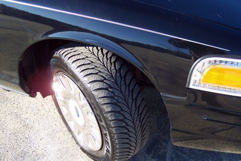 2001 Ford Crown Victoria - The front wheel and fender of a black sedan are shown, with a clear view of the tire tread and the vehicle's turn signal.