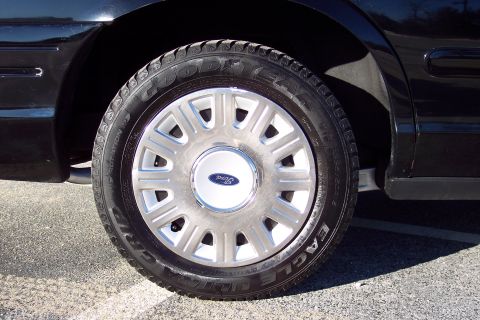 2001 Ford Crown Victoria - Close-up of a black car's wheel a Ford-branded hubcap and Goodyear Eagle tires.