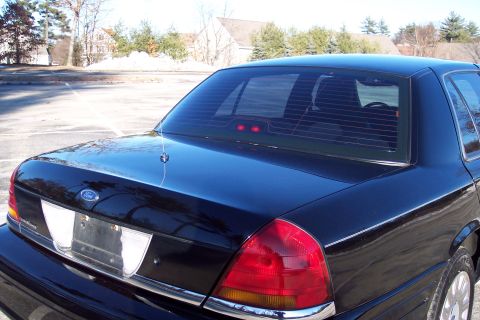 2001 Ford Crown Victoria - Rear view of a black 2001 Ford Crown Victoria parked in a lot with houses in the background.