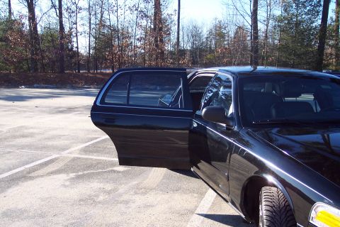 2001 Ford Crown Victoria - A black 2001 Ford Crown Victoria is parked in a lot with its doors open.