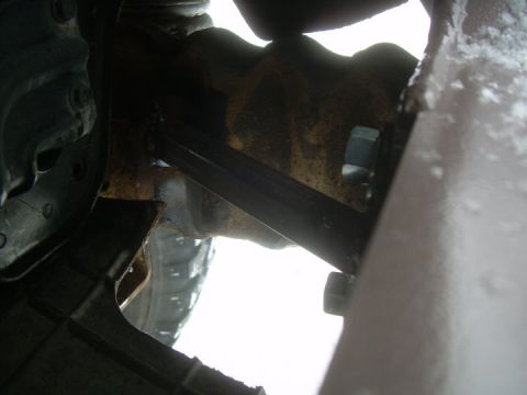1995 Ford Bronco - Tight, dimly lit view up into a truck's frame rail area showing a heavily surface-rusted frame section with a black diagonal brace running…