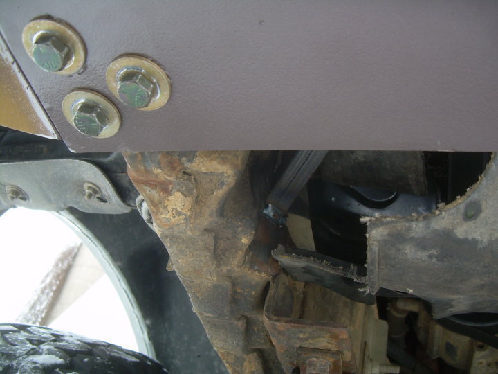 Underside of gray steel truck bumper bolted to rusty frame with hex bolts