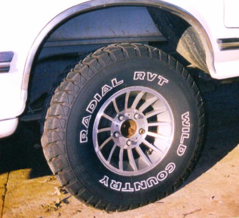 1989 Ford Bronco - Close-up of a tire and wheel assembly on a white vehicle, with visible text on the tire's sidewall.