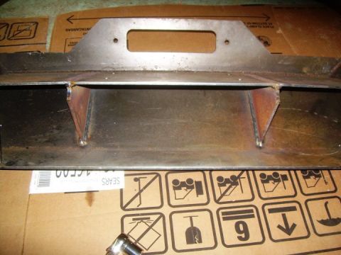 1995 Ford Bronco - Overhead view of a fabricated bare-steel bumper laid on a Sears cardboard box, showing a rectangular license-plate cutout and two triangula…