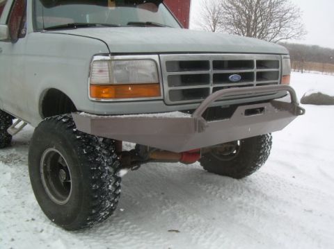 1995 Ford Bronco - Snow-dusted front end of a light gray 1990s Ford truck showing a shop-built bare-steel plate bumper with a tubular grille hoop and a rectan…