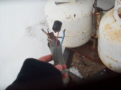 1985 Ford Bronco - A person holds a damaged wiring harness with exposed wires near two large propane tanks in a snowy outdoor setting.