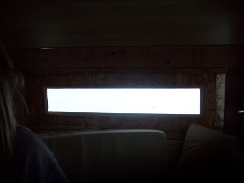 1985 Ford Bronco - The interior of a vehicle shows wood paneling and a wide window looking out.