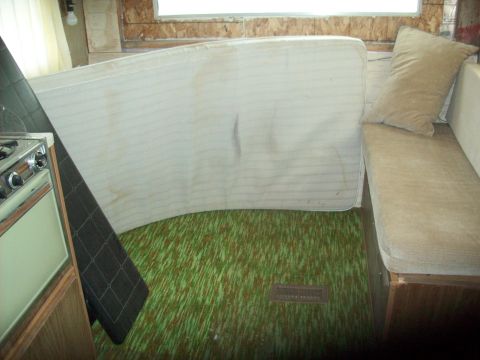 1985 Ford Bronco - The interior of a camper shows a mattress, couch, green carpet, and a stove, suggesting a living space within a vehicle.