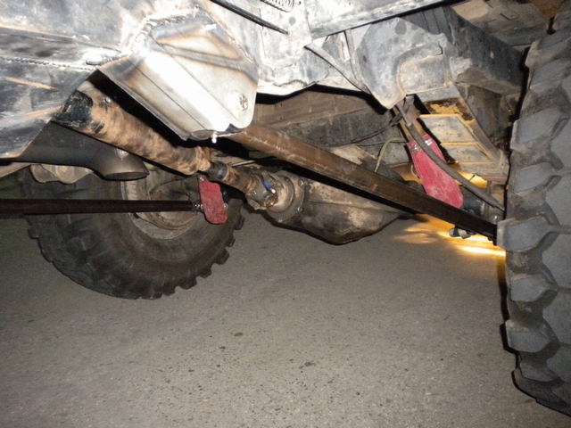 Underside of a lifted 4x4 showing rear axle, driveshaft, fuel tank and red frame brackets