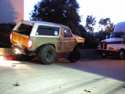 1989 Ford Bronco - Modified Ford Bronco with oversized tires sits beside a semi-truck at dusk.