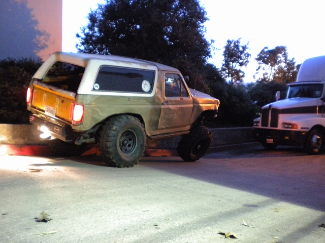 Tan full-size Ford Bronco at dusk, rear 3/4, parked next to a Kenworth semi