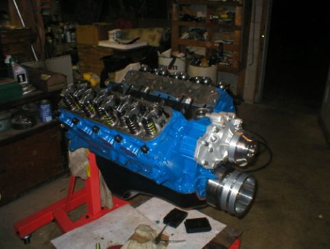 1978 Ford Bronco - A blue V8 engine is mounted on a red stand, ready for installation or work in a cluttered garage setting.