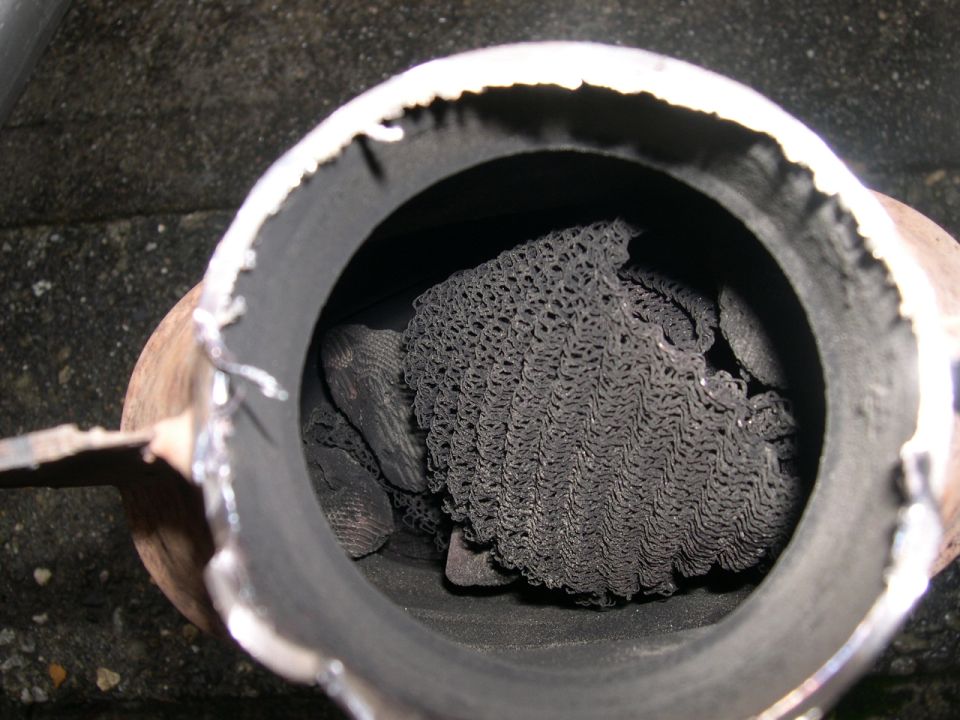 Cut-open catalytic converter showing broken, soot-covered honeycomb substrate inside the shell