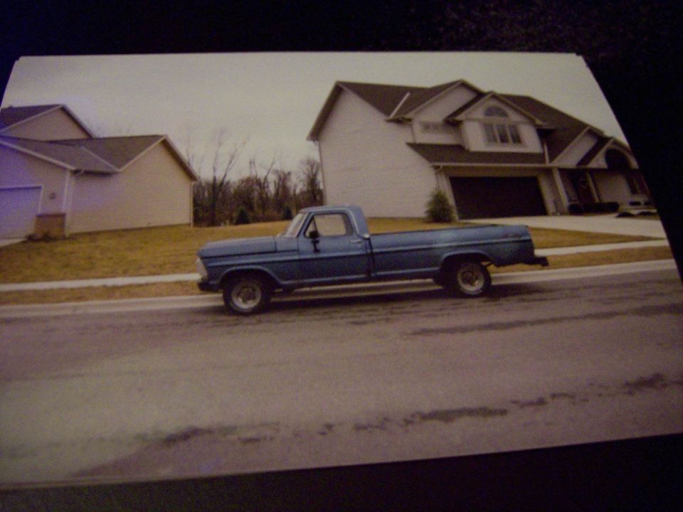 Blue Ford F-100 pickup parked curbside in side view in front of suburban houses