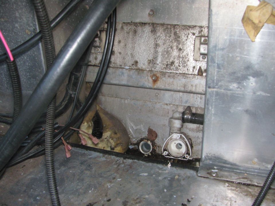 Boat bilge compartment with black wiring, white pump fitting, spray foam, and mildewed aluminum panels