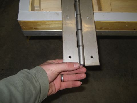 1996 Ford Bronco - A hand is shown holding a metal hinge that is attached to a wooden structure with metal trim.