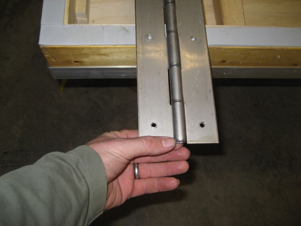 Hand holding a metal hinge attached to a wooden box-like structure