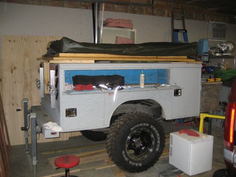 1996 Ford Bronco - A utility truck bed is modified with storage compartments and a tarp, parked indoors.