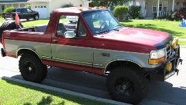 1995 Ford Bronco - This two-tone red and silver Ford Bronco is equipped with off-road lights and large tires, parked on a suburban street.