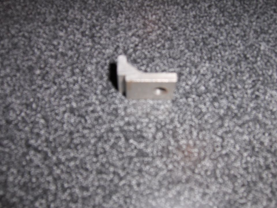 Close-up of a small metal bracket with a hole in it, resting on a speckled gray surface