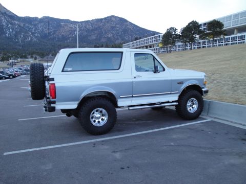 1995 Ford Bronco - A two-tone white and silver Ford Bronco is parked in a lot with mountains in the background.