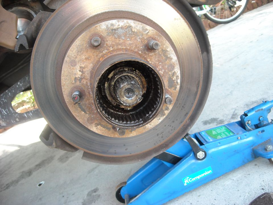 Front wheel hub assembly with a rusty brake rotor, supported by a blue hydraulic jack