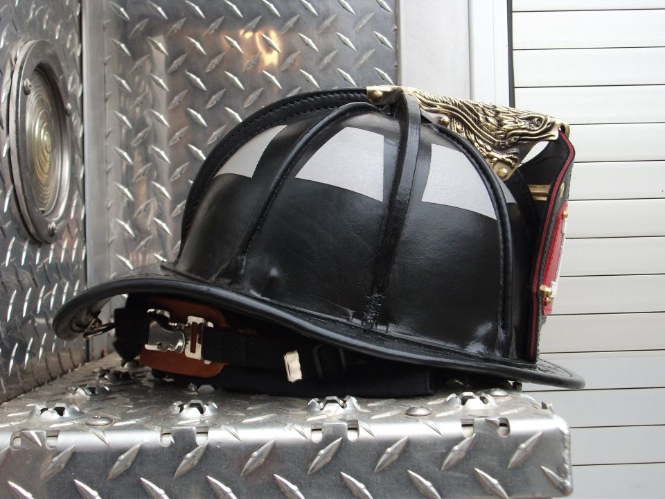 Black leather firefighter helmet with brass eagle on diamond-plate surface