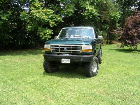 1993 Ford Bronco - 1993 Ford Bronco with lifted suspension sits on a grassy lawn in front of trees.