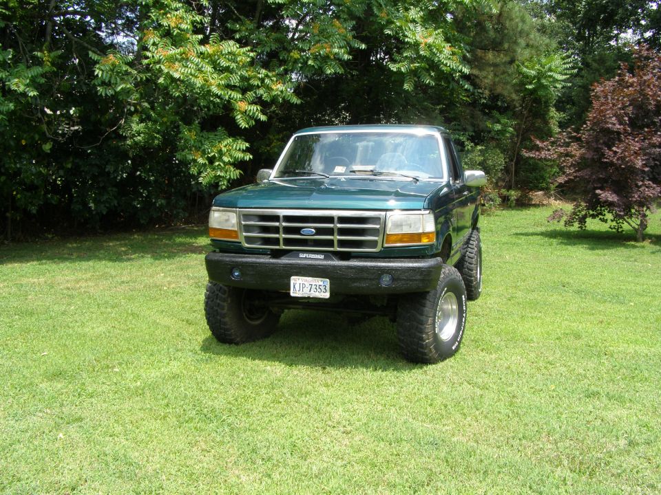 Green 1993 Ford Bronco with lifted suspension parked on grass