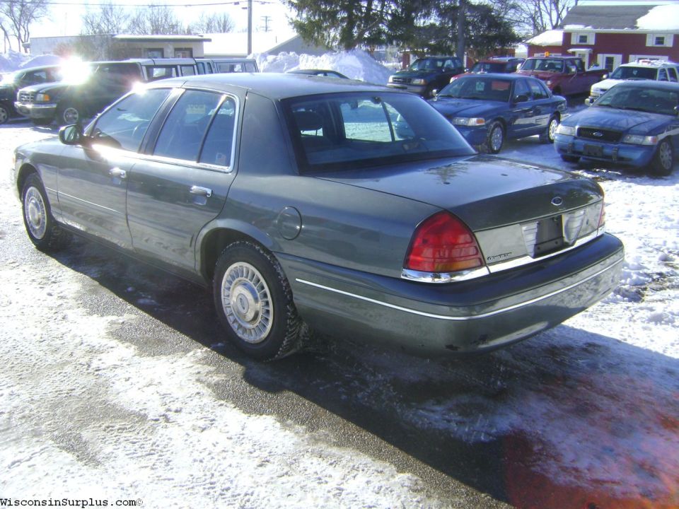 Gray Ford Crown Victoria sedan parked on snow at a surplus auction lot, rear three-quarter view