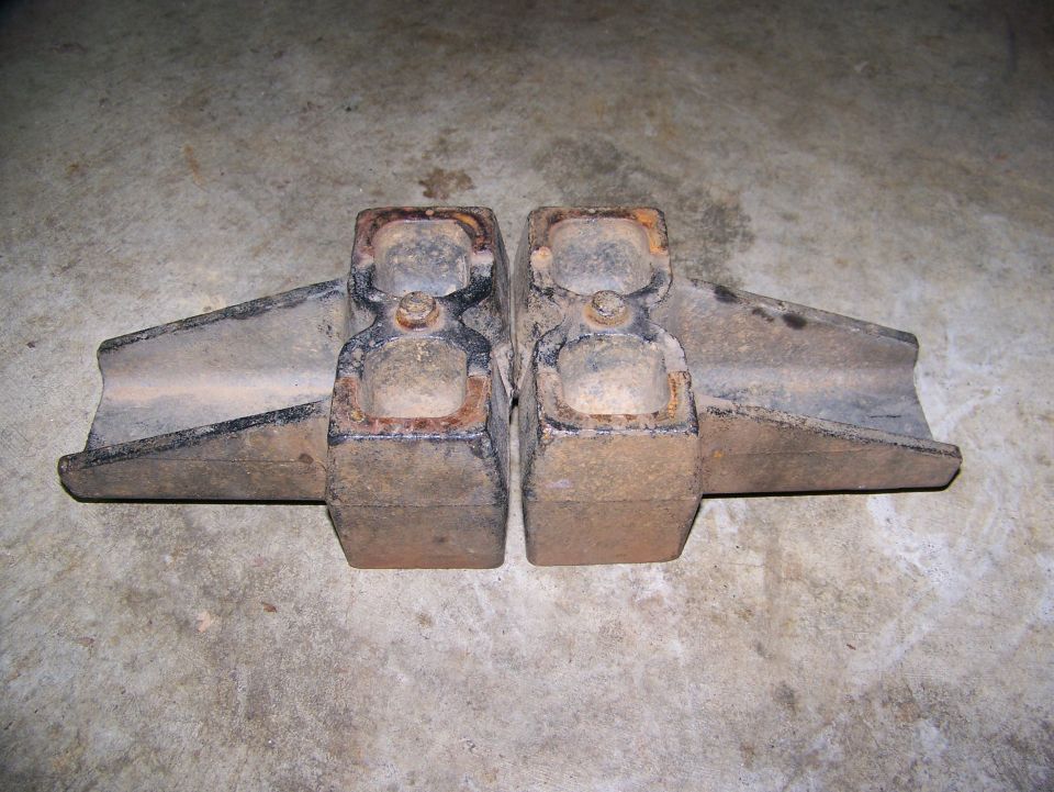 Two rusty cast iron suspension spring perch castings on concrete floor