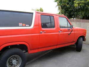1986 Ford Bronco - Side view of a red extended cab pickup truck with a white camper shell.