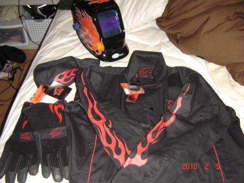 1993 Ford Bronco - New welding gear, including a helmet, jacket, pants, and gloves, is laid out on a bed, all decorated with a red flame motif.
