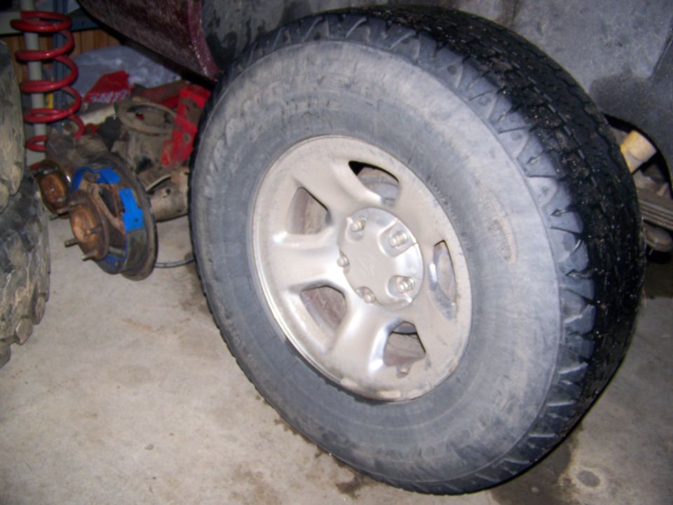 Close-up of a vehicle's wheel and some disassembled suspension components, including a red coil spring and brake parts
