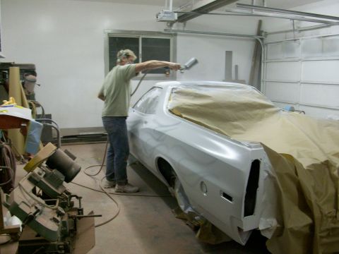 1973 Ford Ranchero - A person is spray painting a vehicle that is covered in masking paper inside a garage.