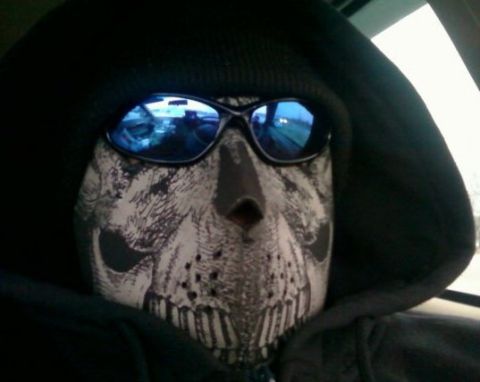 2000 Mercury Grand Marquis - A person wearing a skull mask and sunglasses is visible inside a vehicle, with the dashboard and road reflected in the sunglasses.
