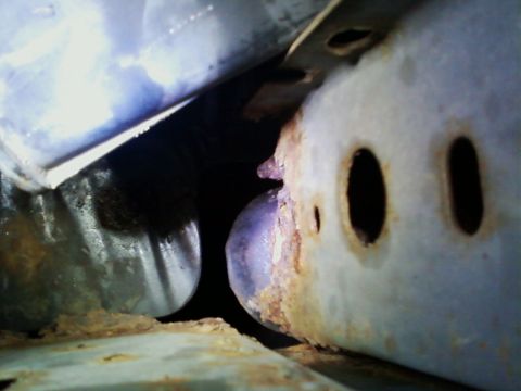 1990 Ford Bronco - Close-up view of a heavily rusted metal component, likely from the underside of a vehicle, showing signs of significant wear and corrosion.