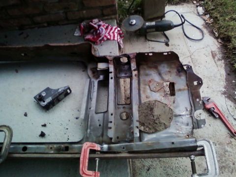 1990 Ford Bronco - A rusted radiator core support is shown with a grinder and wrench nearby, indicating repair work.