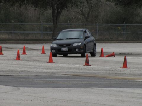 2003 Mazda Protege - Dark hatchback navigates an autocross course marked by orange traffic cones.