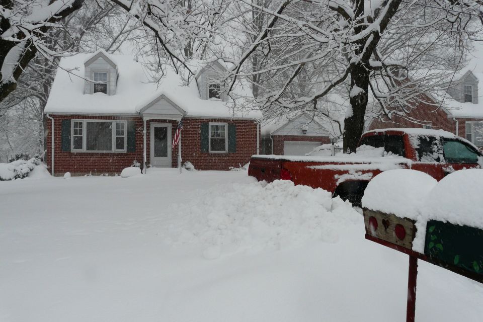 Red pickup truck buried in deep snow at the curb in front of a brick house