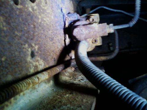 1990 Ford Bronco - Close-up of corroded vehicle components, including brake lines and a protective hose.