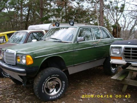 1979 Ford F-250 - A modified green sedan with large off-road tires and roof-mounted lights sits parked outdoors.