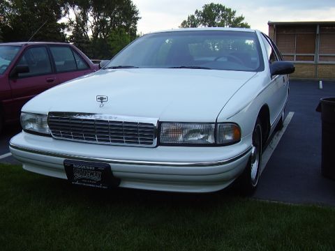 1996 Ford F-150 - A white sedan is parked in a lot, with another car visible to its left and a building in the background.