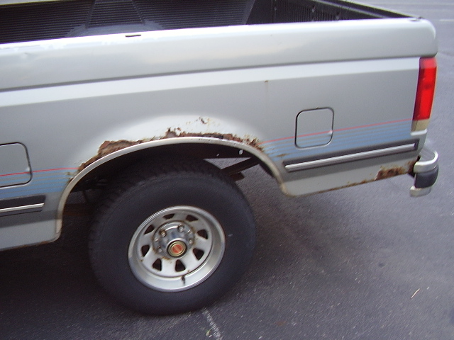 Silver 1996 Ford F-150 pickup truck rear quarter panel with rust around wheel well and bumper