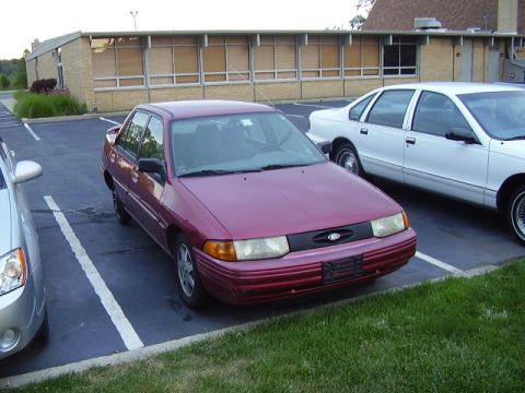 1996 Ford F-150 - A maroon sedan with a Ford badge is parked in a lot next to another vehicle.