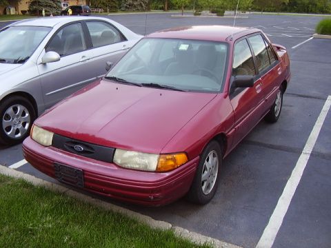 1996 Ford F-150 - Red sedan with a Ford emblem parked in a lot next to another car.