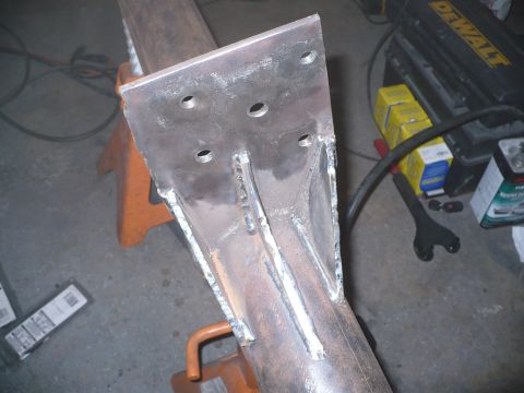 1979 Ford Bronco - A close-up view of a custom metal bracket welded onto a pipe, resting on an orange jack stand.